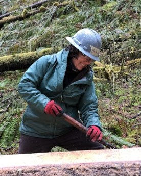 Volunteer smiles while debarking a log in the Oregon woods.